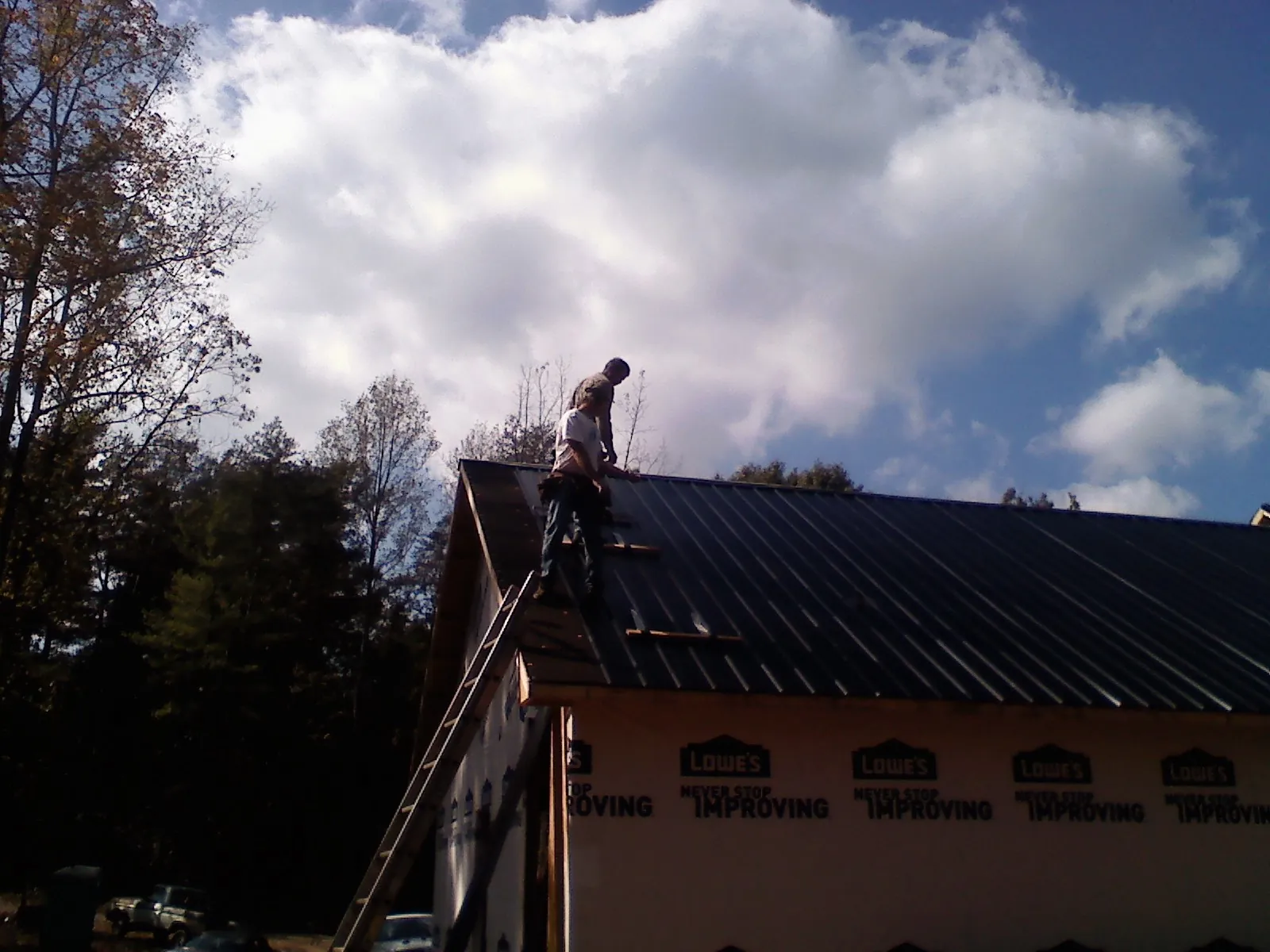 Roofer fastening dark metal panels high against a cloudy sky, from a Roof Inspection job in Cummings