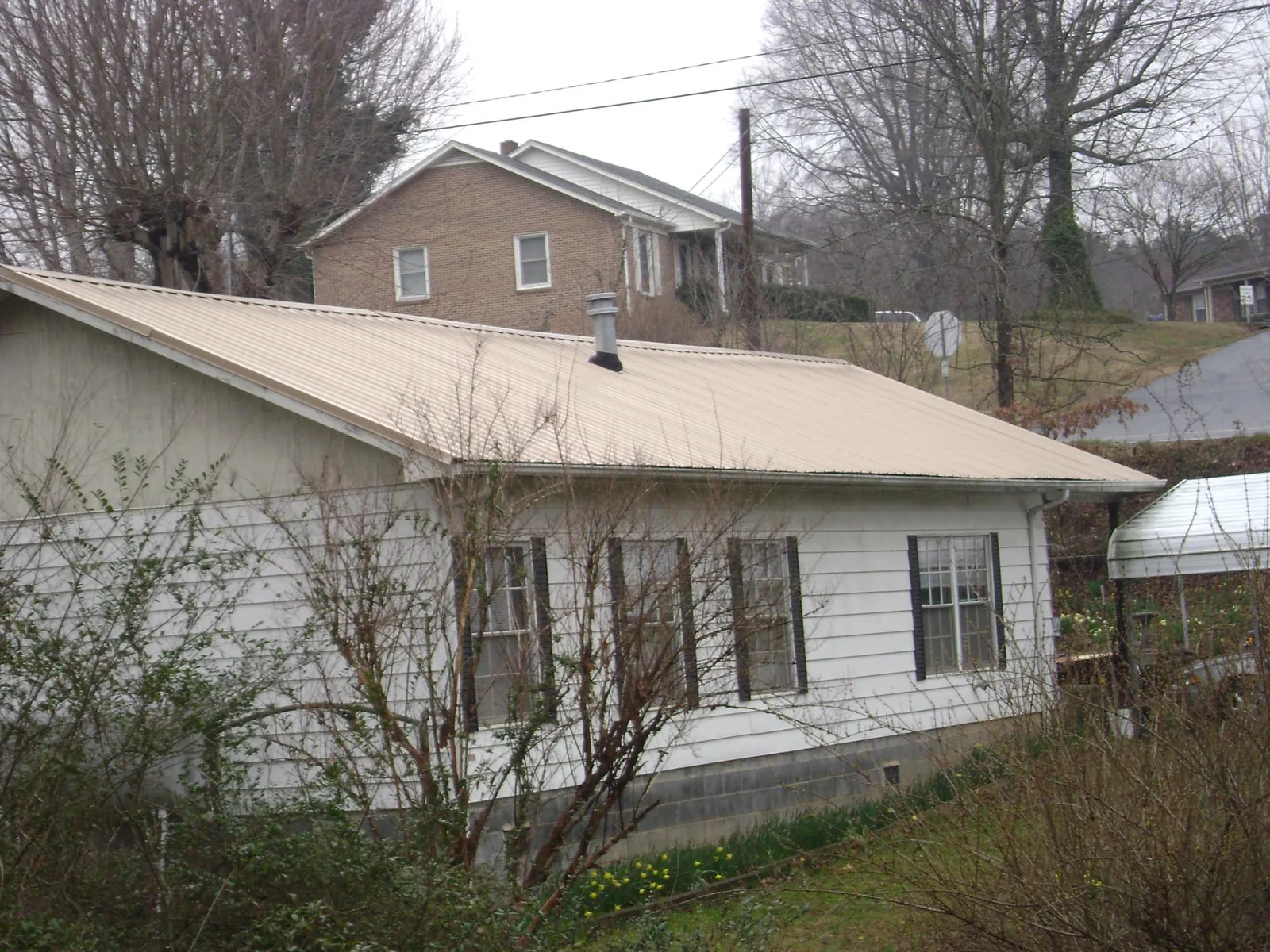 Tan metal roof on a white sided house set into a hillside — Commercial Roofing by Roofing Brothers in Cummings