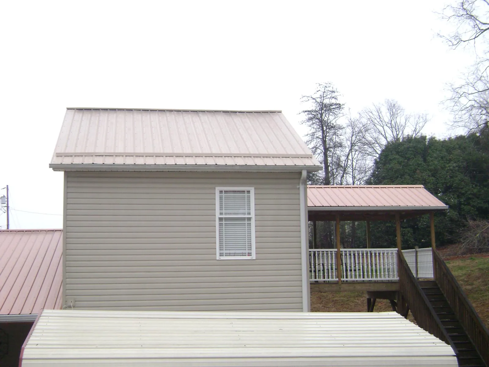 Tan metal roofs on a two story addition and attached porch, from a Roof Replacement job in Cummings